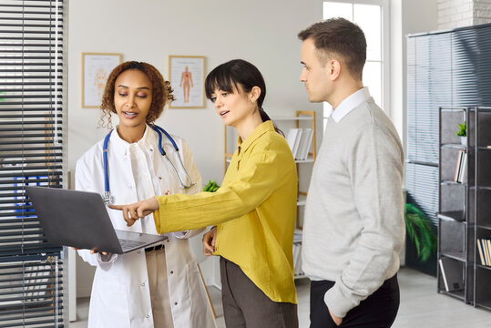 Couple doctor consultation about pregnancy planning and fertility. Woman points to laptop while physician shares results at appointment discussion. Concept family healthcare guidance and support.