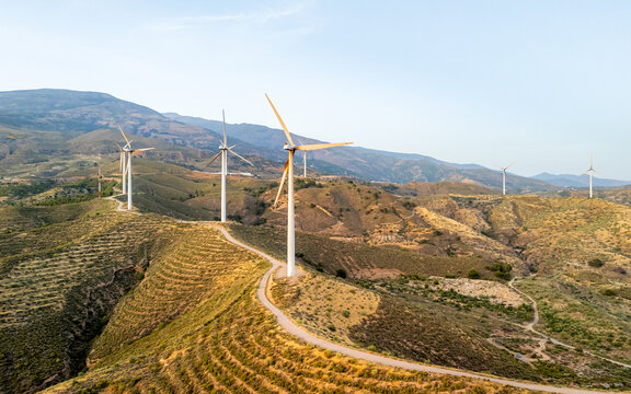 Aerial view of wind turbines standing on a ridge with a winding road through the hilly landscape of Velez de Benaudalla, Andalusia, Spain.