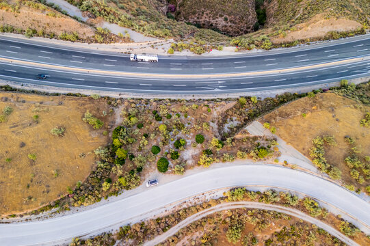 Aerial view of a highway winding through the arid, hilly landscape of Andalusia with a truck and car driving along the road, Velez de Benaudalla, Andalusia, Spain.