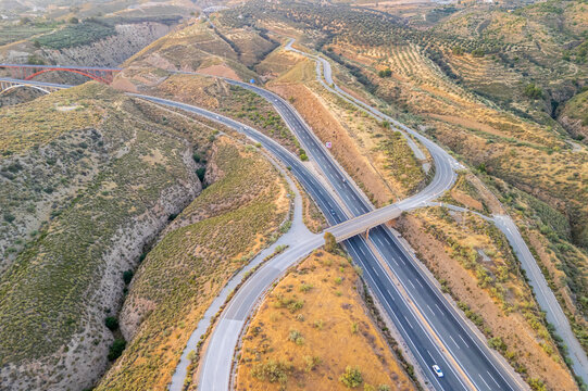 Aerial view of a highway interchange winding through the arid hills and olive groves of the Andalusian countryside in Velez de Benaudalla, Andalusia, Spain.