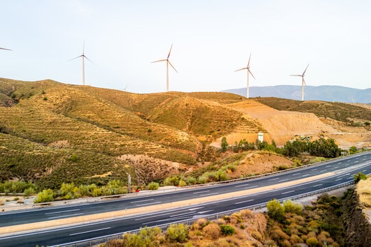 Aerial view of wind turbines on rolling hills above a highway in the dry landscape of Velez de Benaudalla, Andalusia, Spain.