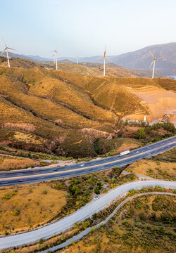 Aerial view of wind turbines on a sunlit hillside overlooking a highway with vehicles in Velez de Benaudalla, Andalusia, Spain.