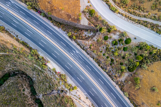 Aerial view of a modern highway cutting through the arid landscape with asphalt lanes and road markings in Velez de Benaudalla, Andalusia, Spain.