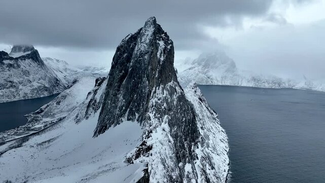 Aerial view of the snow-covered Segla mountain peak rising above the dark waters of the fjord in Senja, Troms, Norway.