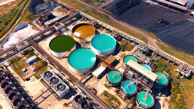 Aerial view of circular storage tanks at plant. Multiple colored liquid tanks stand among complex metal pipelines at facility.