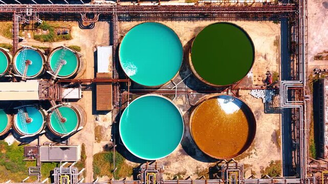 Top down view of colored industrial water tanks. Four large circular tanks containing distinct colored liquids sit within metal pipeline grid.
