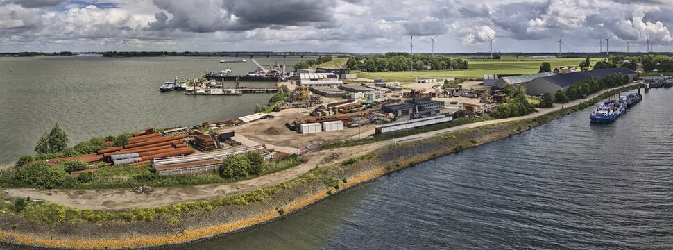 Moerdijk, Netherlands - 05 June 2026: Aerial view of the Moerdijk harbor mouth featuring a maritime contractor's yard, industrial equipment, and ships on the Hollandse Diep river under a cloudy sky.