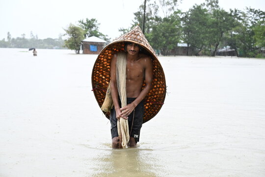 Banshkhali Upazila, Chittagong Division, Bangladesh - 09 July 2026: View of a man wearing a traditional conical hat and carrying a fishing net while wading through floodwaters in a rural area.