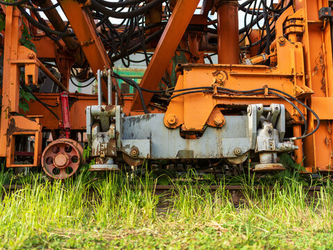 View of the orange industrial machinery at the Railway Museum Outdoors Exposition with rusty metal components and wheels set amidst green grass in Vilnius, Vilniaus apskritis, Lithuania.