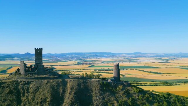 Aerial view of Hazmburk castle ruins on a hilltop with surrounding fields and clear blue sky in Klapy, Usti nad Labem Region, Czechia.