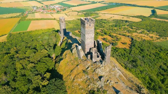 Aerial view of the historic Hazmburk castle ruins perched on a rocky hill surrounded by vast agricultural fields and green forests in Klapy, Usti nad Labem Region, Czechia.