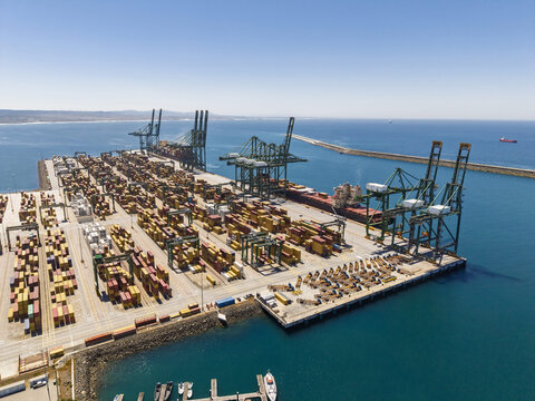Aerial view of the Port of Sines container terminal featuring rows of colorful shipping containers, large gantry cranes, and a cargo ship docked in Sines, Setubal, Portugal.