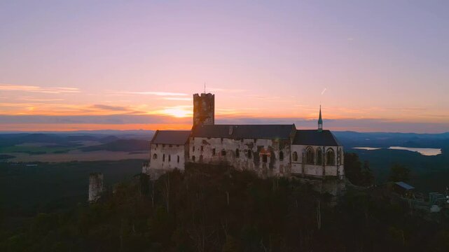 Aerial view of State Castle Bezdez at sunset with golden light illuminating the historic stone walls and surrounding landscape in Bezdez, Liberecky kraj, Czechia.