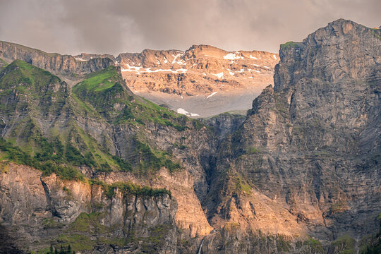 View of the dramatic limestone cliffs and steep mountain walls of Cirque du Fer a Cheval, with patches of snow and lush green slopes in Sixt-Fer-a-Cheval, Auvergne-Rhone-Alpes, France.