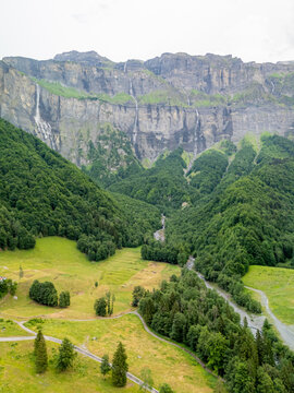 View of the dramatic limestone cliffs and cascading waterfalls of Cirque du Fer a Cheval surrounded by lush green forests and mountain meadows in Sixt-Fer-a-Cheval, Auvergne-Rhone-Alpes, France.