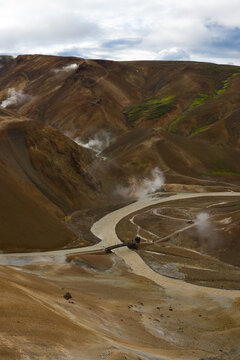 Aerial view of Kerlingarfjoll geothermal area with steaming vents, a winding river, and colorful volcanic mountains under a cloudy sky, Hella, Hrunamannahreppur, Iceland.