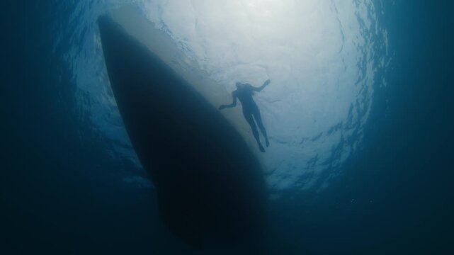 Woman swims nearby the sailing boat as seen from the bottom of the ocean