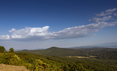 Scenic panoramic landscape of green forest hills under blue sky with dramatic white clouds