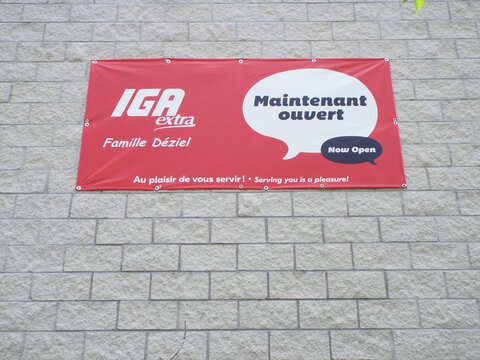 Gatineau, Quebec, Canada &ndash; June 16, 2026: A red banner with "IGA extra Famille D&eacute;ziel" text displays Maintenant ouvert and Now Open on a light brick wall on Chem. Vanier.
