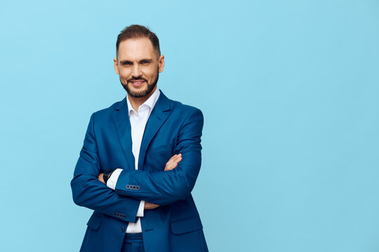 A professional businessman stands with arms crossed against a solid blue background, conveying confidence, poise, clarity, focus, and calm emotion in a clean studio portrait.
