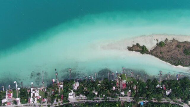 Aerial view of the turquoise waters of Bacalar Lagoon with wooden docks, a small island, and lush vegetation along the shoreline in Bacalar, Quintana Roo, Mexico.