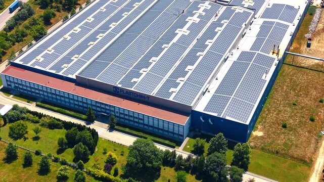 Industrial facility rooftop with solar panel installation. Aerial view shows rows of photovoltaic arrays mounted on a blue factory building.