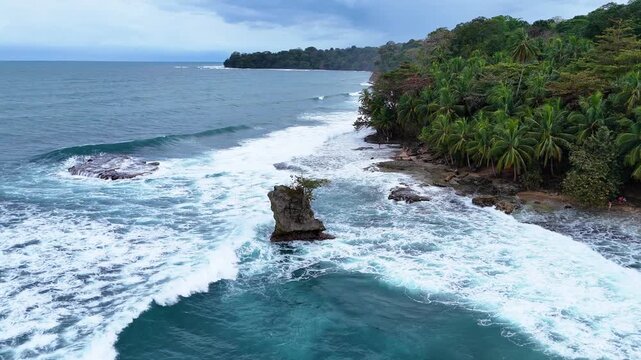 Aerial view of Refugio Nacional Gandoca-Manzanillo with lush tropical forest and waves crashing against the rocky coastline in Limon, Costa Rica.