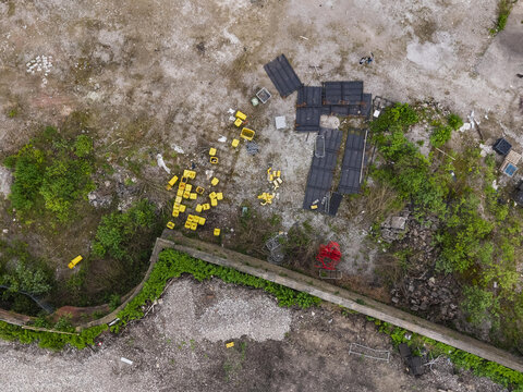 Aerial view of an industrial waste site with scattered yellow plastic crates, discarded black panels, and overgrown vegetation near a concrete wall in Manchester, England, United Kingdom.