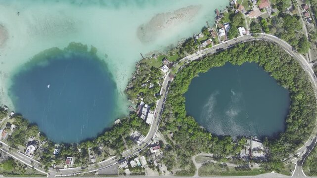 Aerial view of the turquoise waters of Bacalar lagoon and its surrounding cenotes with lush vegetation and a coastal road in Bacalar, Quintana Roo, Mexico.