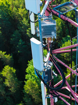 Aerial view of a telecommunications tower with antennas and cables set against a dense green forest in Riga, Latvia.