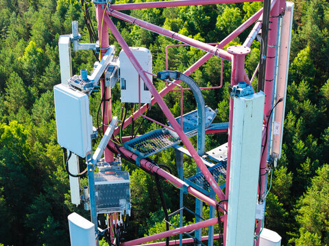 Aerial view of a telecommunications tower with antennas and equipment mounted on a metal structure, surrounded by a dense green forest in Riga, Latvia.