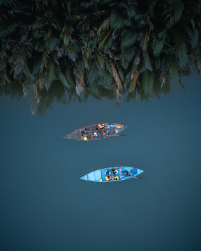Aerial view of two small boats carrying people in life jackets on the river near the lush palm trees of the Lantern Riverside in Hoi An, Da Nang, Vietnam.