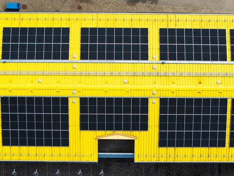 Aerial view of a bright yellow industrial building roof featuring large arrays of solar panels in Valdlauci, Kekavas novads, Latvia.