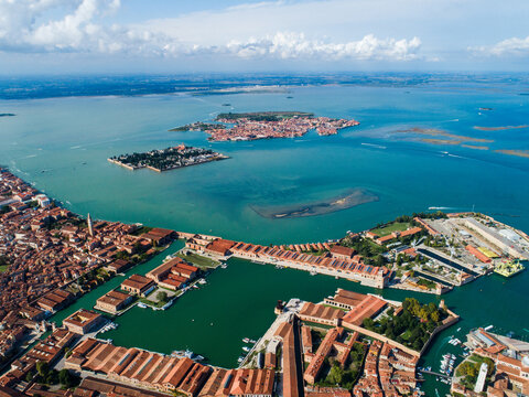 Aerial view of the historic Venetian Arsenal with its distinctive red-tiled rooftops, shipyard basins, and surrounding canals in the lagoon of Venice, Veneto, Italy.