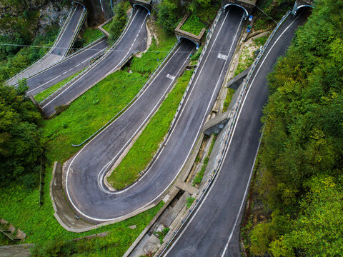 Aerial view of San Boldo Pass featuring its iconic hairpin bends carved into mountain tunnels surrounded by lush green slopes in Cison di Valmarino, Veneto, Italy.