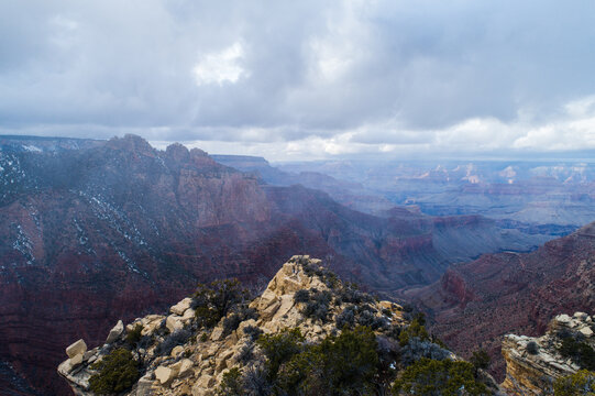Aerial view of the Grand Canyon with rugged rock formations, sparse vegetation, and a cloudy sky in Coconino County, Arizona, United States.