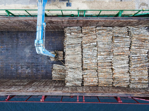 Aerial view of a crane loading timber logs into the cargo hold of a ship at the port in Riga, Latvia.