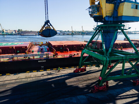 Riga, Latvia - 24 September 2022: Aerial view of a large industrial crane loading cargo onto a ship at the port with a worker walking on the dock under clear blue skies.