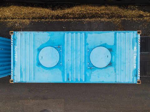 Aerial view of a blue shipping container with two circular hatches on its roof, positioned in a freight yard in Riga, Latvia.