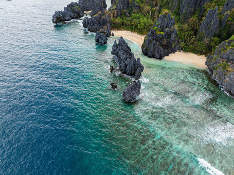 Aerial view of Hidden Beach featuring jagged limestone rock formations rising from turquoise waters and a sandy shoreline in El Nido, Mimaropa, Philippines.