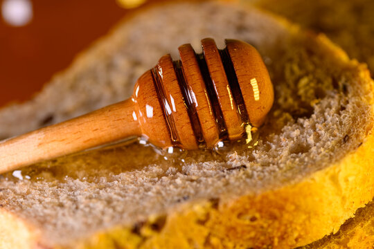 Golden honey and fresh bread slices beside glass jar in warm rustic kitchen setting