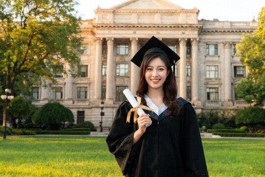 Smiling Asian Graduate With Diploma in Front of University