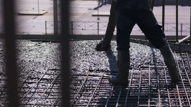 Worker pouring concrete over reinforcing mesh for floor slab close up