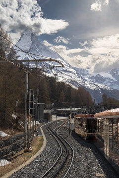 View of the Gornergrat railway train tracks leading towards the snow-capped Matterhorn peak under a bright sky in Zermatt, Valais, Switzerland.