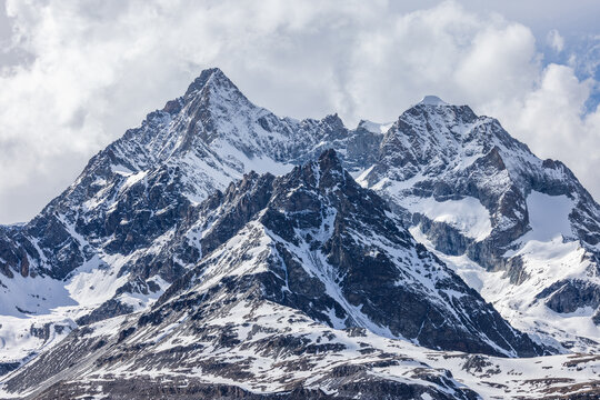 View of the snow-capped peaks of the Gornergrat mountain range in the Swiss Alps, featuring rugged rocky ridges, glaciers, and a cloudy sky in Zermatt, Valais, Switzerland.