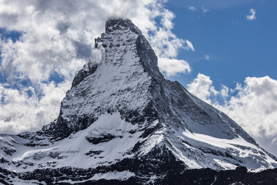 View of the iconic Matterhorn mountain peak with its snow-capped pyramid shape rising against a bright blue sky with scattered white clouds in Zermatt, Valais, Switzerland.