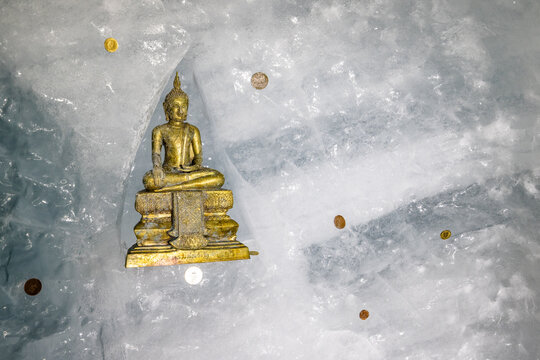 View of a golden Buddha statue placed on the icy surface of the Matterhorn Glacier Paradise with scattered coins in Zermatt, Wallis, Switzerland.