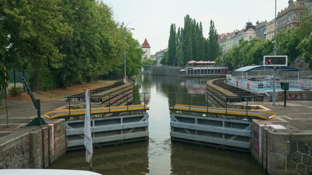 Smichov Lock gates open for a tourist cruise boat on Vltava River in Prague, Czechia. Hydraulic water lock mechanism guides navigation. European river channel waterway travel background scene.