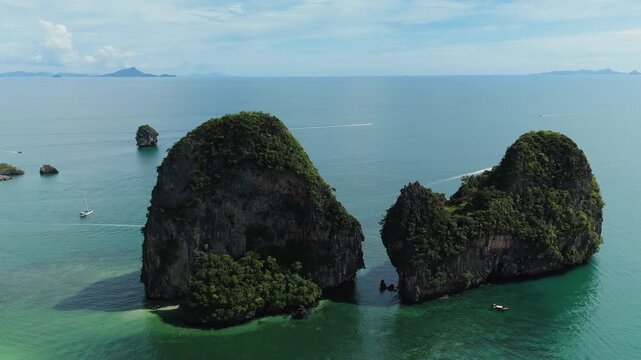 Aerial view of limestone karsts rising from the turquoise sea with lush green vegetation and small boats in Phuket, Thailand.