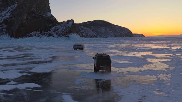 Aerial view of vehicles driving across the vast frozen surface of Lake Baikal during a golden sunset in Khuzhir, Irkutsk Oblast, Russia.